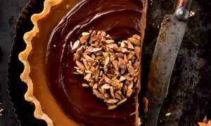 Herzförmige Schoko Tarte mit Karamell und gehackten Mandeln, daneben ein altes Messer.