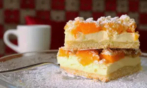 Zwei Stücke Mandarinen Schmand Kuchen Blech auf einem Teller, bestäubt mit Puderzucker. Im Hintergrund eine weiße Tasse.