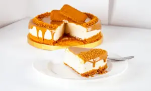 Ein Stück cremiger Lotus Cheesecake mit Karamell und Keksbröseln auf einem Teller, daneben der ganze Kuchen.