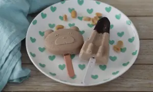 Zwei niedliche Eis am Stiel, ein Bär und eine Rakete, mit Erdnussbutter-Geschmack, liegen auf einem Teller mit grünen Herzen.