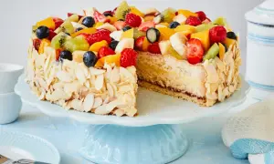 Eine einfache Torte, verziert mit frischen Früchten wie Erdbeeren, Kiwi und Blaubeeren, umgeben von Mandelblättchen.