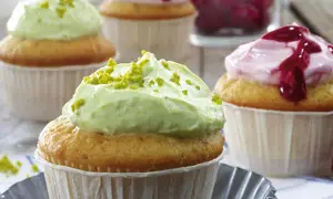 Zwei Cupcakes mit cremiger, grüner Pistazien-Frosting und ein weiterer mit rosa Beeren-Frosting.
