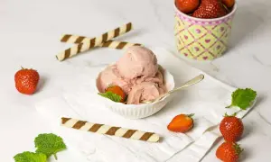 Ein Schälchen cremiges italienisches Erdbeereis, garniert mit frischen Erdbeeren und Minze. Dazu knusprige Waffelröllchen.