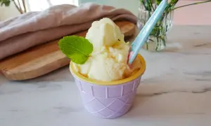 Ein cremiges Ananas Eis in einem lila Becher, garniert mit Minze. Perfekt für heiße Tage!