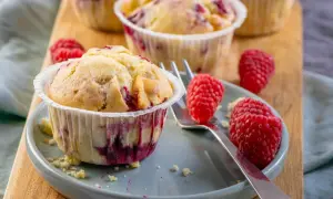Saftige Himbeer Muffins auf einem Teller, garniert mit frischen Himbeeren. Ein Genuss für jeden Kaffeetisch.