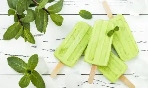 Erfrischendes Minzeis selber machen: Grüne Eis am Stiel mit frischer Minze und Eiswürfeln auf weißem Holzuntergrund.