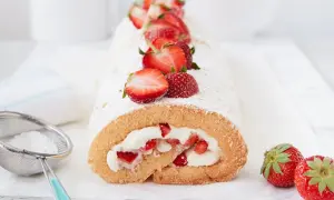 Saftige erdbeer biskuitrolle mit frischen Erdbeeren und Puderzucker bestäubt, daneben ein Sieb mit Puderzucker.