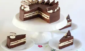 Schokoladentorte mit cremiger Füllung und Schokostückchen, inspiriert von der Kinder Pingui Torte. Serviert auf einem Tortenständer mit einzelnen Tortenstücken.
