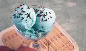 Ein Glas mit engelblauem Eis, bestreut mit Schokostreuseln und bunten Zuckerperlen, steht auf einem Bambusteller.
