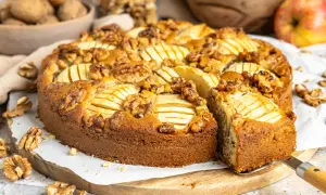 Ein saftiger Apfel Walnuss Kuchen, dekoriert mit Apfelscheiben und ganzen Walnüssen, wird auf einem Holzbrett präsentiert.
