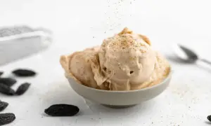 Schüssel mit cremigem Tonka Eis, bestreut mit gemahlenen Tonkabohnen. Dunkle Tonkabohnen liegen verstreut auf dem Tisch.