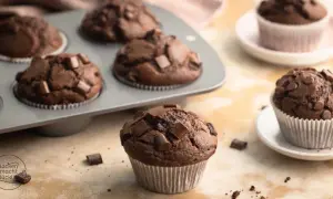 Schokomuffins mit Schokostückchen, perfekt für Kinder. Ein Muffin liegt vorne, weitere im Blech und auf Tellern.