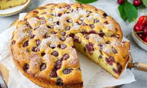 Saftiger Kuchen mit Kirschen, bestäubt mit Puderzucker. Ein Stück wurde bereits herausgeschnitten.