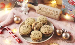 Leckere Nutella Kekse, umhüllt von gehackten Nüssen, liegen auf einem Teller. Ein Nudelholz mit der Aufschrift "Backe, backe Kuchen" und Weihnachtsdeko sorgen für festliche Stimmung.