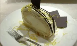 Ein Stück Zitronenrolle mit cremiger Füllung, dekoriert mit Schokoladenglasur und Zitronenzesten. Ein perfektes Zitronenrolle Rezept zum Nachbacken.