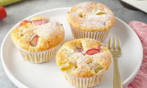 Drei saftige Rhabarber Muffins, mit Puderzucker bestäubt, auf einem weißen Teller. Ein goldener Gabel liegt daneben.