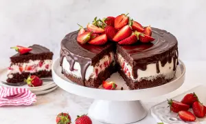 Eine saftige Yogurette Torte mit Schokoladenglasur und frischen Erdbeeren, ein Stück davon ist bereits angeschnitten.