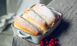 Drei goldbraune Salzburger Nockerl, mit Puderzucker bestäubt, in einer Auflaufform, daneben rote Johannisbeeren.