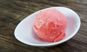 Ein Löffel cremiges Erdbeereis mit Sahne in einer weißen Schale auf Holzhintergrund.