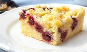 Ein saftiges Stück Kirsch-Streuselkuchen vom Blech, mit vielen Kirschen und knusprigen Streuseln, auf einem weißen Teller.