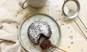 Ein saftiger Schoko-Tassenkuchen ohne Ei, bestäubt mit Puderzucker und Schokostreuseln, bereit zum Genießen.