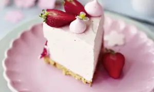 Ein Stück Erdbeer Cheesecake mit frischen Erdbeeren und Baiser-Tupfern auf einem rosa Teller.