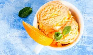 Erfrischendes orangen sorbet in einer Schale, garniert mit Minze und einer Orangenspalte auf blauem Untergrund.