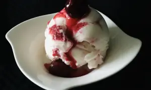 Ein Löffel cremiges Sauereis mit Kirschsauce und einer ganzen Kirsche obendrauf, serviert in einer weißen Schale.