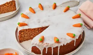 Ein saftiger karottenkuchen ohne mehl, verziert mit Zuckermöhren und Zuckerguss. Ein Stück ist bereits angeschnitten.