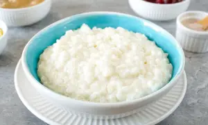 Cremiger Milchreis im blauen Schälchen, daneben Schüsseln mit Apfelmus, Kirschen und Zimt. Perfekt für ein einfaches Milchreis Rezept.