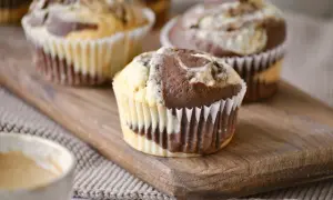 Zwei leckere Marmor Muffins auf einem Holzbrett, daneben eine Tasse Kaffee.