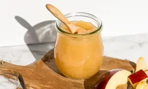Glas mit selbstgemachtem Apfelmus, Holzlöffel und Apfelstücke auf einem Holzbrett mit Zimt.