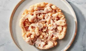 Ein goldbrauner, puderzuckerbestäubter **Funnel Cake** auf einem grauen Teller.