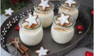 Vier Gläser mit cremigen Parfait-Rezepten im Glas, garniert mit Zimt und Sternenplätzchen. Weihnachtliche Deko mit Zimtstangen und Kugeln.