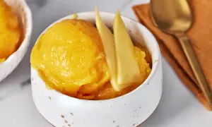 Erfrischendes Mango Sorbet in einer Schale, garniert mit Mangostücken. Daneben ein Löffel auf einem orangen Tuch.