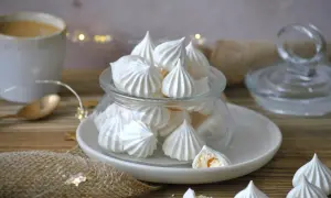 Leckeres Meringen Rezept: zarte Baiser-Häufchen in einem Glas, daneben eine Tasse Kaffee und Lichterkette.