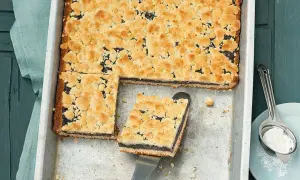 Ein frisch gebackener Mohnkuchen mit Streuseln, wie von Frau Holle. Ein Stück wird gerade herausgehoben.