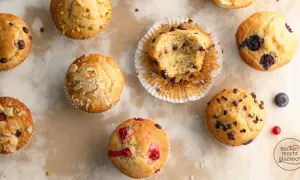 Verschiedene Muffins, die nach einem Muffins Grundrezept gebacken wurden: mit Schokostückchen, Blaubeeren, Himbeeren und Mandeln. Einer ist angeknabbert.