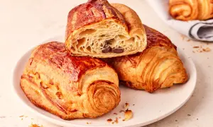 Złociste, chrupiące pain au chocolat na talerzu, jedno przekrojone, ukazujące puszyste wnętrze z kawałkami czekolady.