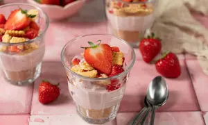 Leckeres Erdbeer-Cheesecake im Glas, geschichtet mit Keksboden und frischen Erdbeeren, garniert mit einer Erdbeerscheibe.
