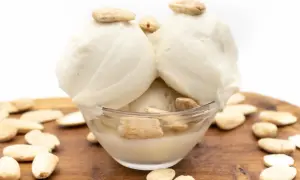 Schüssel mit cremigem Mandeleis, garniert mit Mandeln. Umgeben von ganzen Mandeln auf Holzbrett. Perfekt, um Mandeleis selber machen.