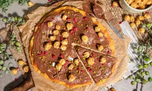 Eine köstliche Nutella Pizza, belegt mit karamellisiertem Popcorn und gehackten Pistazien, bereit zum Genießen.