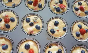 Frisch zubereiteter Teig für Heidelbeer Muffins, mit saftigen Blaubeeren und roten Beeren in einer Muffinform.