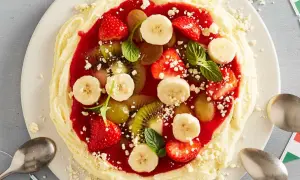 Fruchtige eis pizza mit Erdbeeren, Bananen, Kiwi und Trauben auf cremigem Boden, garniert mit Minze.