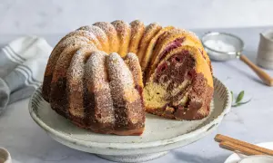 Ein saftiger Marmorkuchen mit Kirschen, bestäubt mit Puderzucker, auf einem rustikalen Kuchenständer.