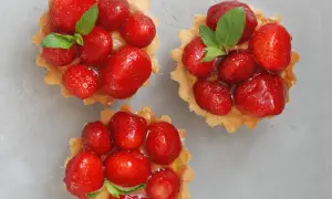 Drei köstliche Erdbeer Tartelettes, garniert mit frischer Minze, auf grauem Untergrund.