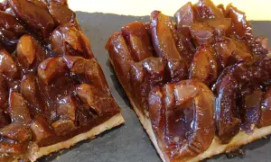 Zwei Stücke saftiger Zwetschgenkuchen vom Blech, glänzend und karamellisiert, auf dunkler Platte angerichtet.