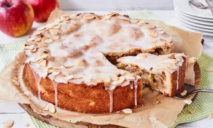 Ein köstlicher gedeckter Apfelkuchen mit zarter Glasur und Mandelblättchen, daneben ein Stück Apfelmus.