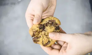 Hände halten einen weichen Chocolate Chip Cookie, der gerade zerbrochen wurde. Das Innere ist voller geschmolzener Schokolade. Ein perfektes soft cookies rezept!