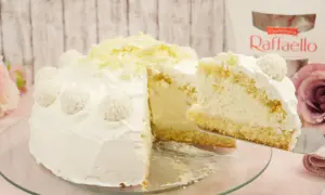 Eine köstliche Raffaello Torte, verziert mit Kokosraspeln und weißer Schokolade. Ein Stück wird gerade serviert.